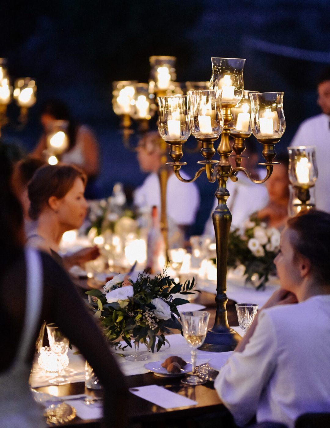 Decorated tables with floral composition and old fashioned candl Decorated tables with floral composition and old fashioned candlesticks and guests in the celebration evening